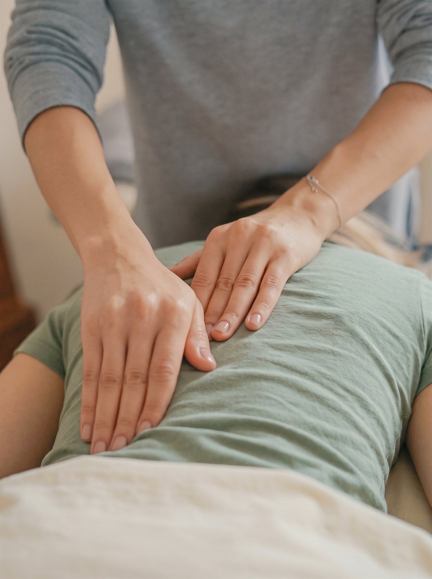 Mains posées sur le bas du dos d’une personne habillée, pendant une séance de microkinésithérapie